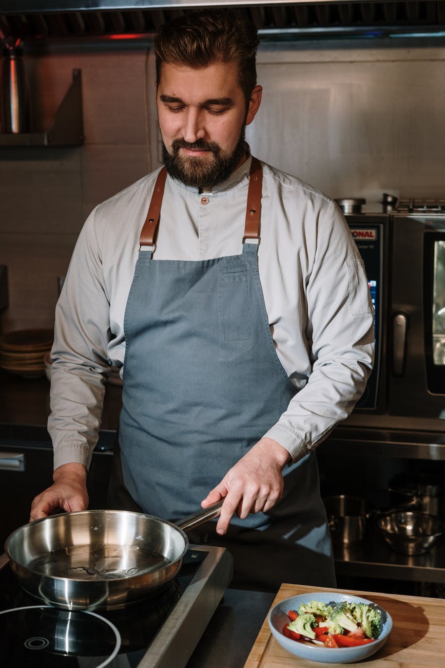 man in blue apron holding stainless steel bowl