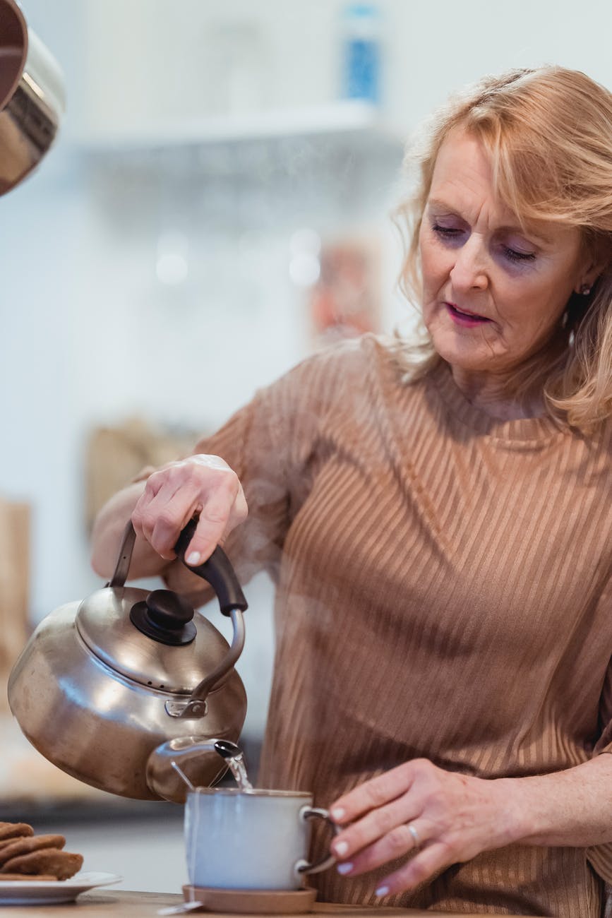 elderly woman preparing tea in house kitchen